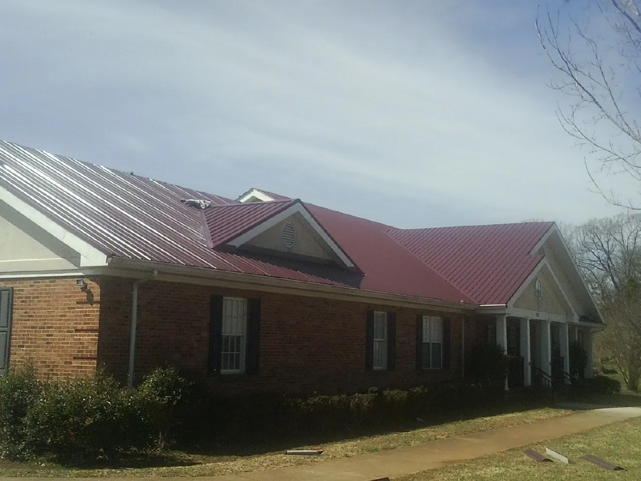 Red metal roof with gabled entries on a long brick building, from a Hail Damage Roof Repair job in Roann