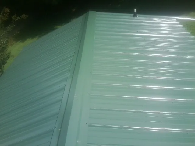 New green metal panels meeting at the ridge of a roof — Flat Roof Repair work by our crew in Roann
