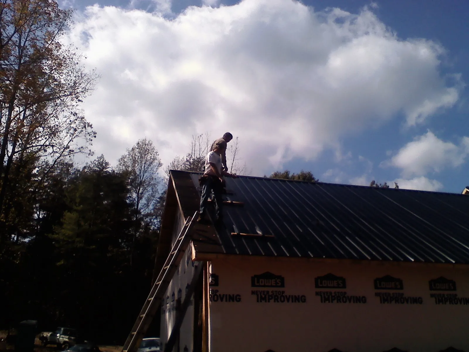 Roofer fastening dark metal panels high against a cloudy sky, from a Roof Inspection job in Roann