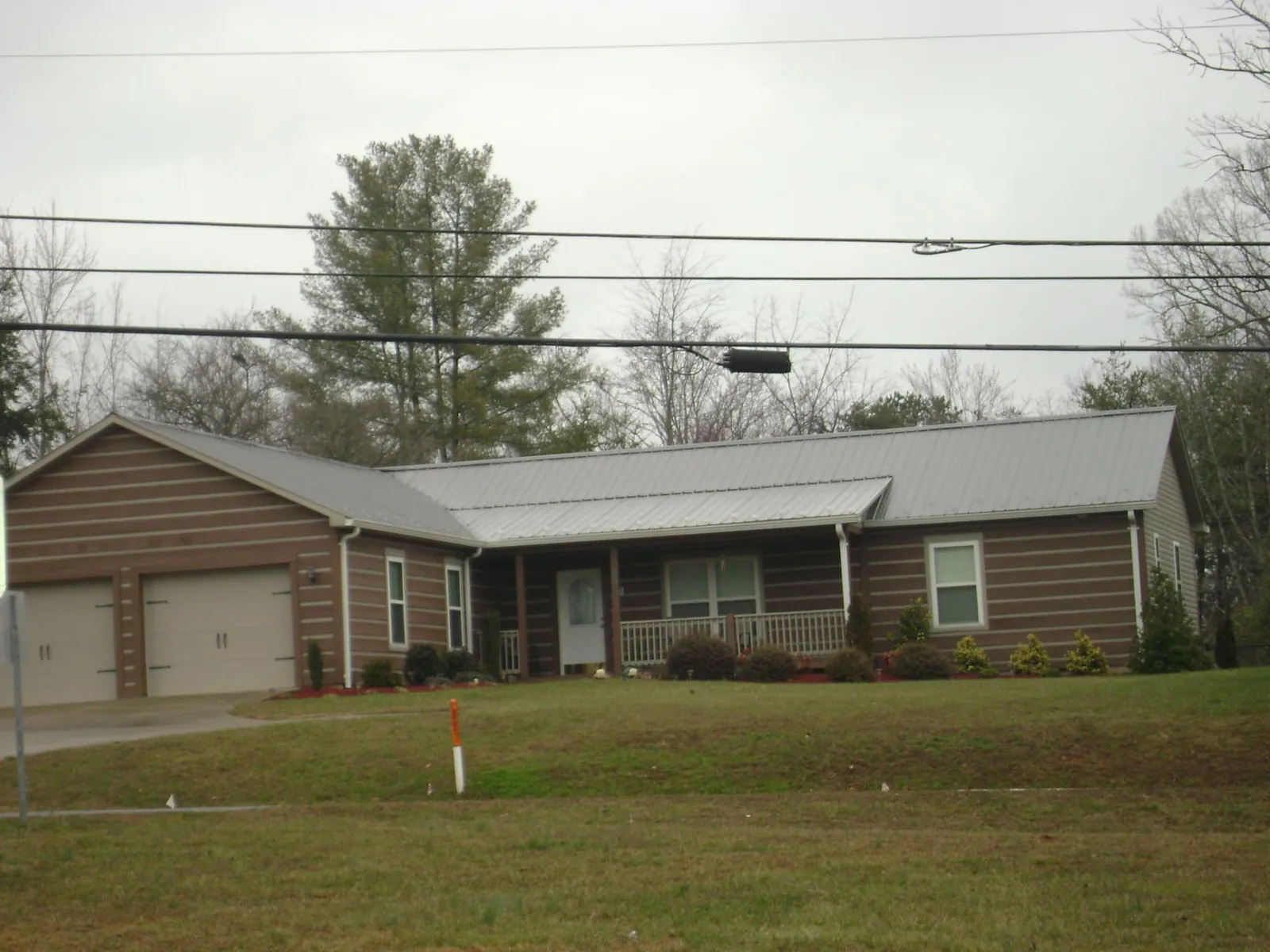 Gray metal roof on a log sided ranch home with a front porch in Roann