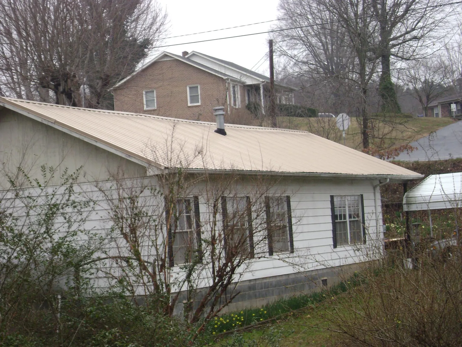 Tan metal roof on a white sided house set into a hillside — Commercial Roofing by Roofing Brothers in Roann