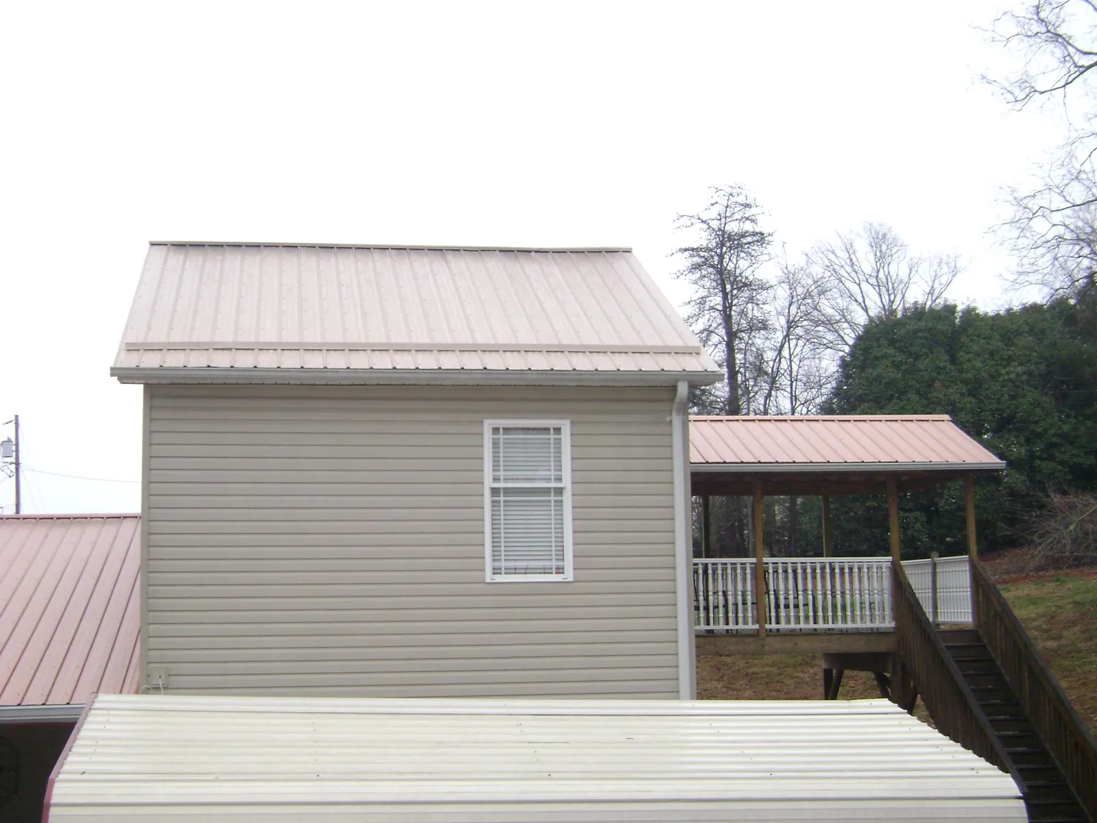 Tan metal roofs on a two story addition and attached porch, from a Roof Replacement job in Roann